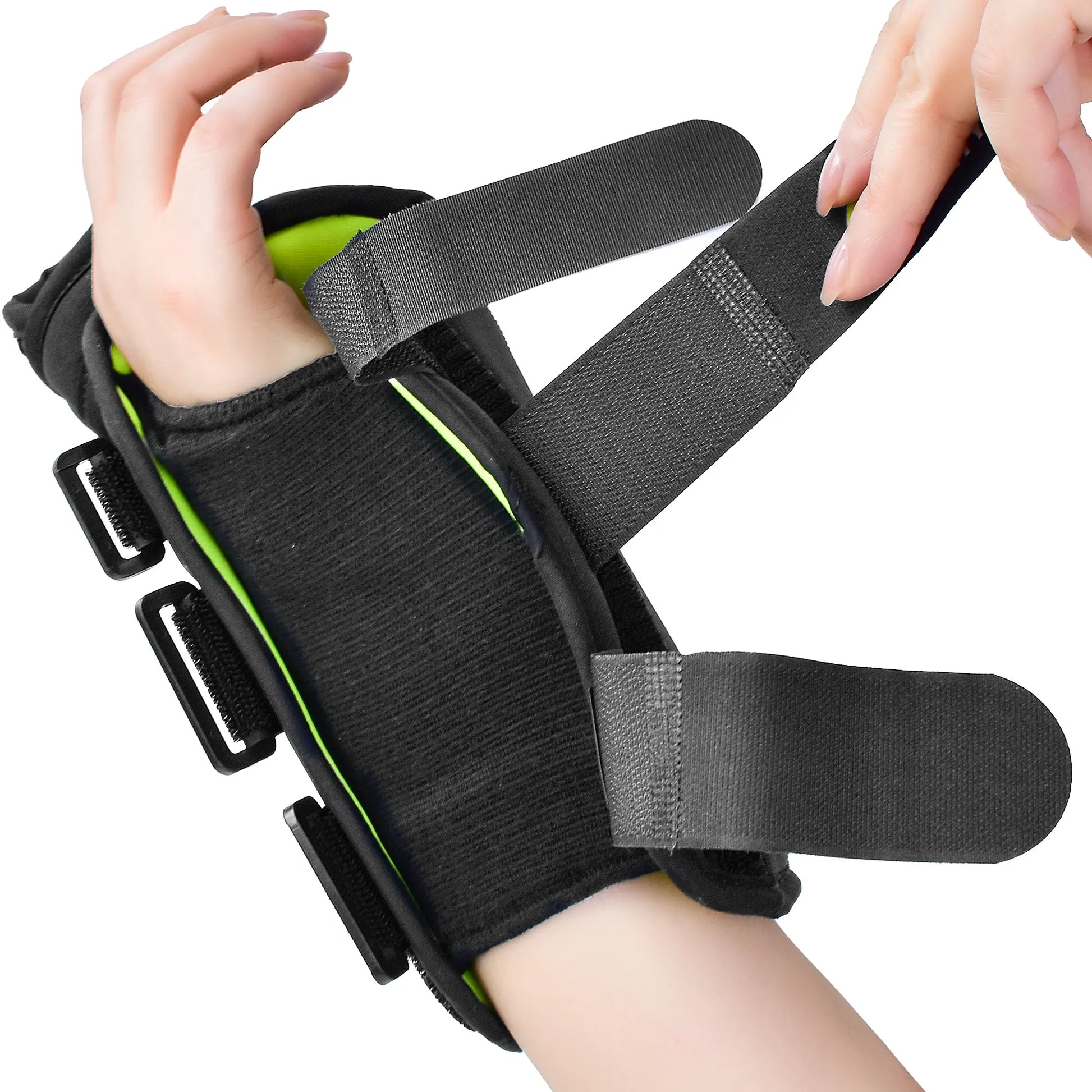 A black wrist support brace with bright green lining and adjustable hook-and-loop straps, shown being worn and adjusted by hands against a white background.
